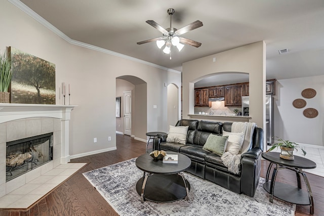 living room featuring ceiling fan, crown molding, a fireplace, and dark hardwood / wood-style flooring