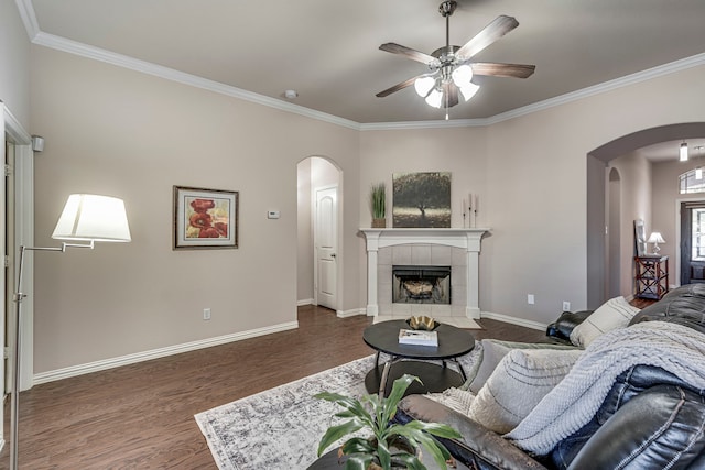 living room featuring ceiling fan, crown molding, dark wood-type flooring, and a tiled fireplace