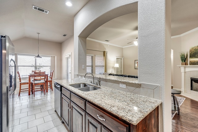 kitchen featuring crown molding, appliances with stainless steel finishes, sink, light stone countertops, and a tile fireplace