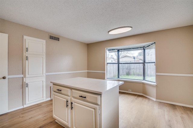 kitchen featuring a textured ceiling, a center island, built in desk, white cabinetry, and light hardwood / wood-style floors