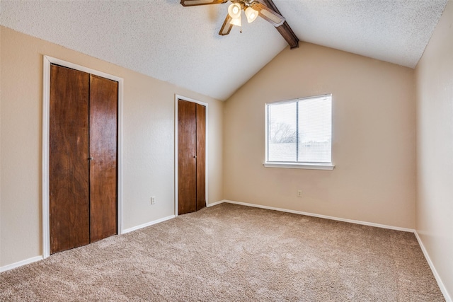 unfurnished bedroom with lofted ceiling with beams, carpet floors, a textured ceiling, and ceiling fan