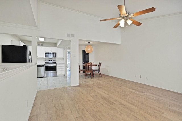 kitchen with high vaulted ceiling, white cabinets, appliances with stainless steel finishes, and crown molding