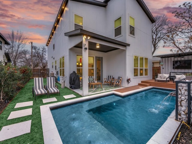 back house at dusk featuring pool water feature, a patio, and outdoor lounge area