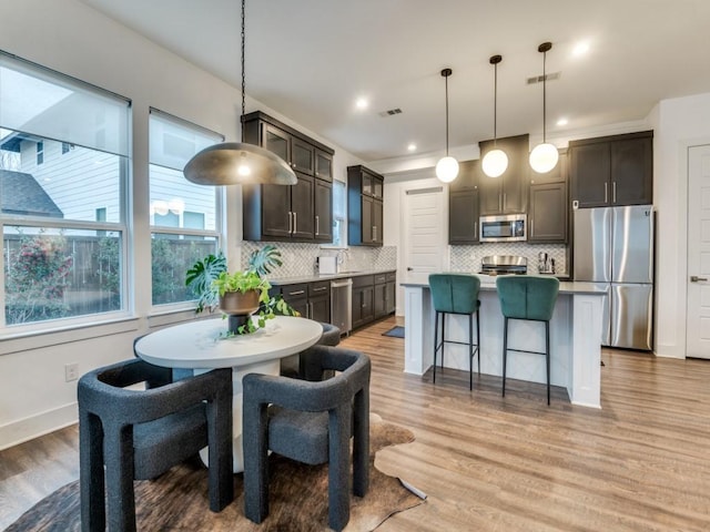 kitchen with a center island, light hardwood / wood-style floors, dark brown cabinets, pendant lighting, and stainless steel appliances