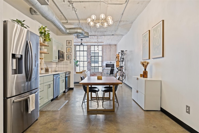 kitchen featuring decorative backsplash, appliances with stainless steel finishes, concrete floors, and a notable chandelier