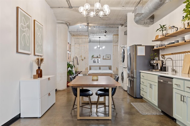 kitchen featuring hanging light fixtures, appliances with stainless steel finishes, sink, green cabinetry, and stacked washer / dryer