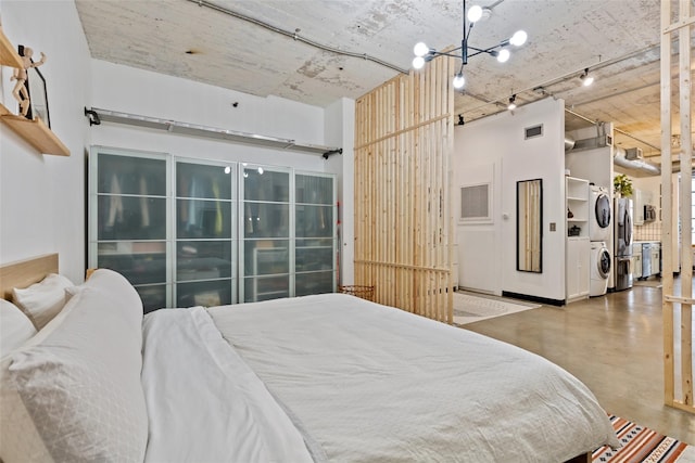 bedroom with stainless steel fridge, concrete floors, a spacious closet, stacked washer / dryer, and a chandelier