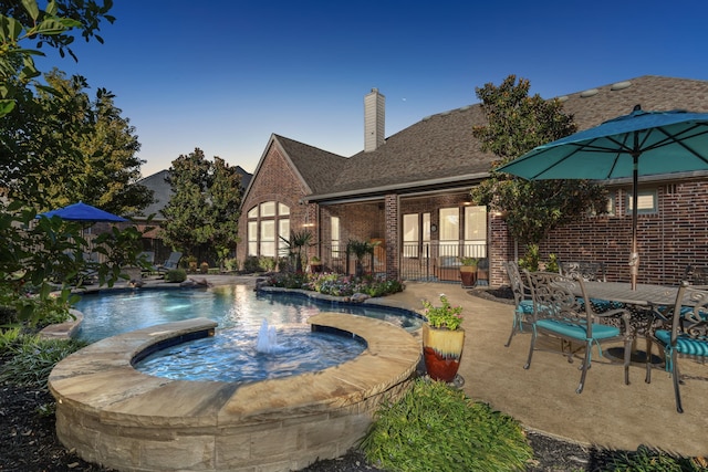 pool at dusk with pool water feature, an in ground hot tub, and a patio area