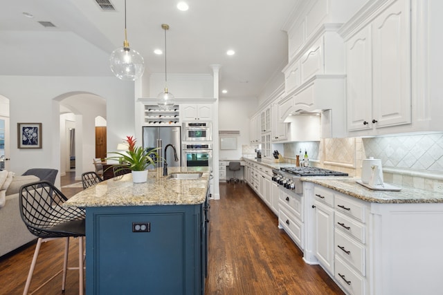 kitchen with a kitchen breakfast bar, appliances with stainless steel finishes, decorative light fixtures, white cabinetry, and a kitchen island with sink