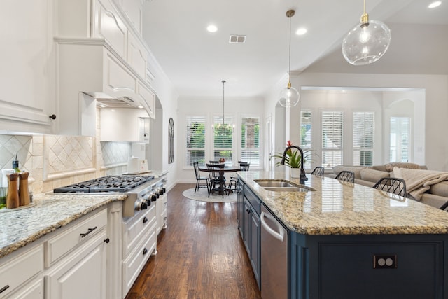 kitchen with white cabinetry, stainless steel appliances, decorative backsplash, sink, and a center island with sink