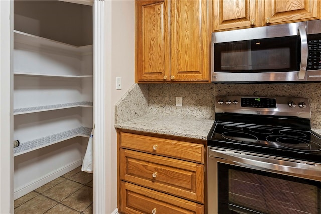 kitchen featuring tasteful backsplash, light tile patterned floors, light stone countertops, and stainless steel appliances