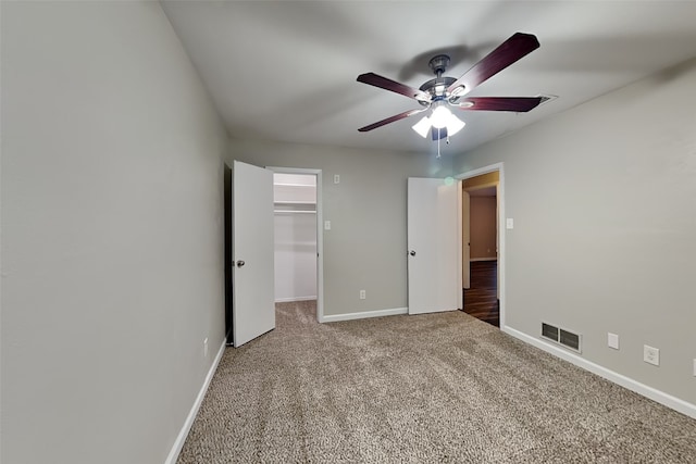 unfurnished bedroom with a closet, ceiling fan, a spacious closet, and carpet floors