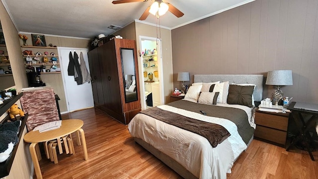 bedroom featuring crown molding, ceiling fan, ensuite bath, light hardwood / wood-style floors, and wooden walls