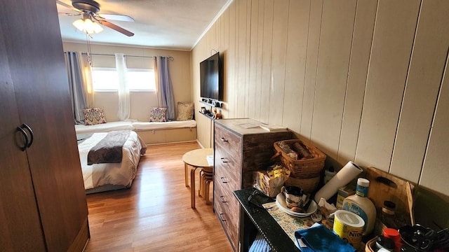 bedroom with ceiling fan, wood walls, crown molding, and light hardwood / wood-style floors