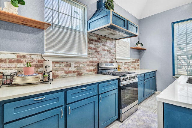 kitchen featuring lofted ceiling, premium range hood, blue cabinets, stainless steel range with gas stovetop, and brick wall