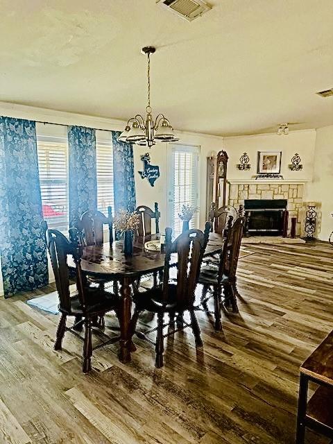 dining space with hardwood / wood-style flooring, plenty of natural light, a stone fireplace, and an inviting chandelier