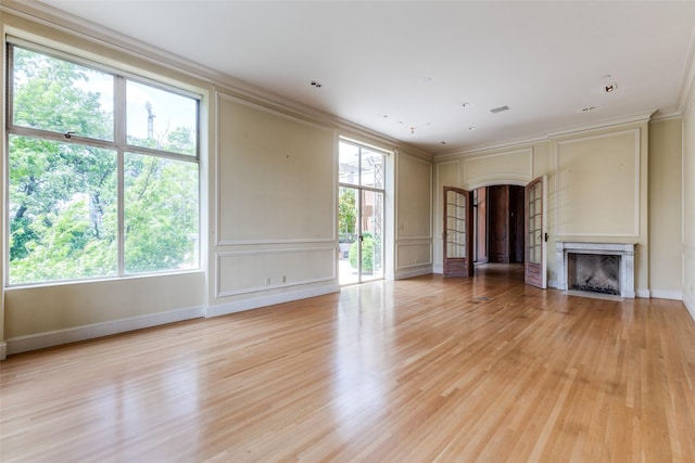 unfurnished living room with light hardwood / wood-style flooring, ornamental molding, and a healthy amount of sunlight