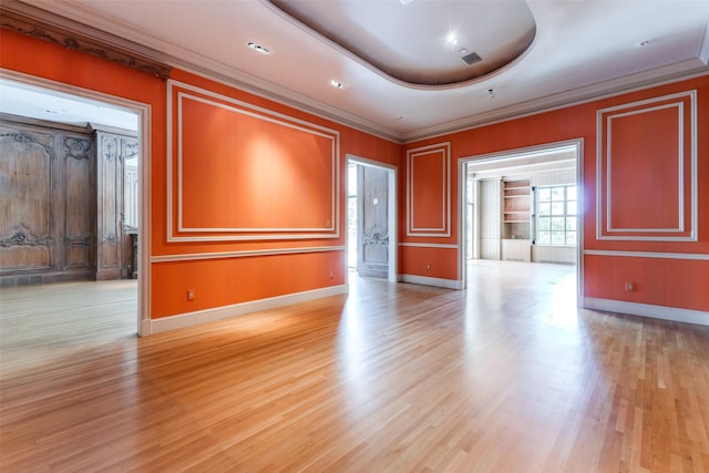 empty room featuring ornamental molding, light wood-type flooring, and a raised ceiling