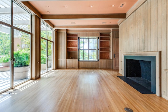 unfurnished living room featuring built in features, beamed ceiling, light hardwood / wood-style flooring, and wooden walls