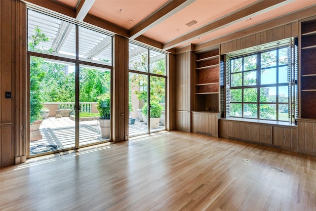 spare room with built in features, light wood-type flooring, beamed ceiling, and a wealth of natural light