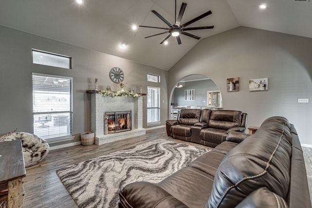 living room with ceiling fan, high vaulted ceiling, a fireplace, and wood-type flooring