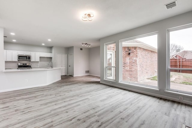 unfurnished living room featuring plenty of natural light, sink, and light hardwood / wood-style floors