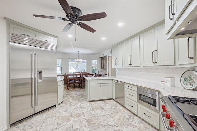 kitchen with sink, hanging light fixtures, built in appliances, tasteful backsplash, and kitchen peninsula