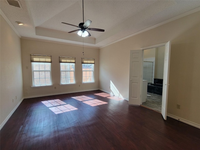 empty room featuring ornamental molding, a tray ceiling, dark hardwood / wood-style flooring, and a textured ceiling