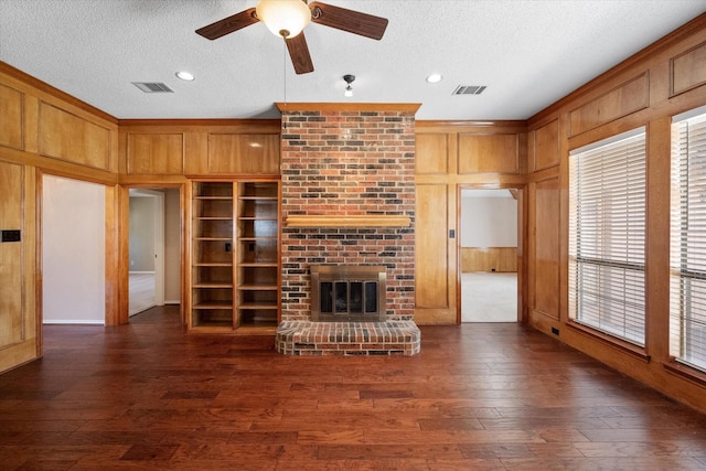 unfurnished living room with built in features, dark wood-type flooring, a textured ceiling, and a brick fireplace