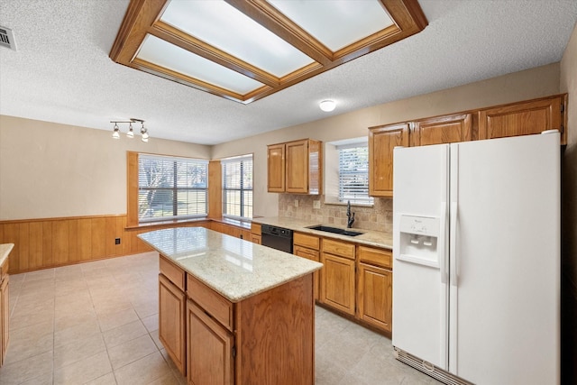 kitchen featuring white refrigerator with ice dispenser, sink, light stone counters, a center island, and black dishwasher