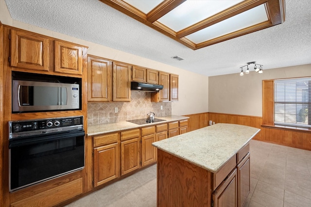 kitchen with a textured ceiling, light tile patterned floors, black appliances, and a center island