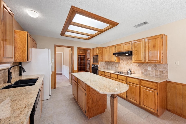 kitchen with a textured ceiling, black appliances, a center island, tasteful backsplash, and sink