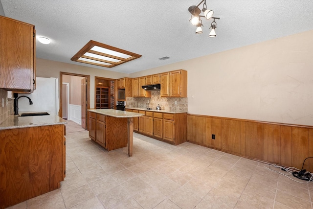 kitchen featuring a textured ceiling, black appliances, a kitchen island, sink, and backsplash