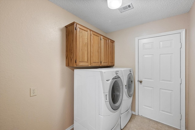 clothes washing area with light tile patterned flooring, cabinets, a textured ceiling, and washing machine and clothes dryer