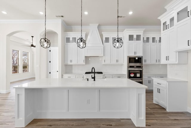 kitchen featuring decorative light fixtures, appliances with stainless steel finishes, a center island with sink, and ornamental molding