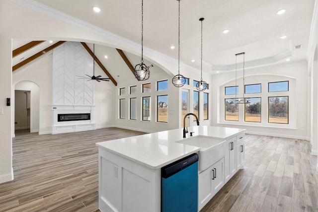 kitchen featuring dishwashing machine, white cabinets, decorative light fixtures, a fireplace, and a center island with sink