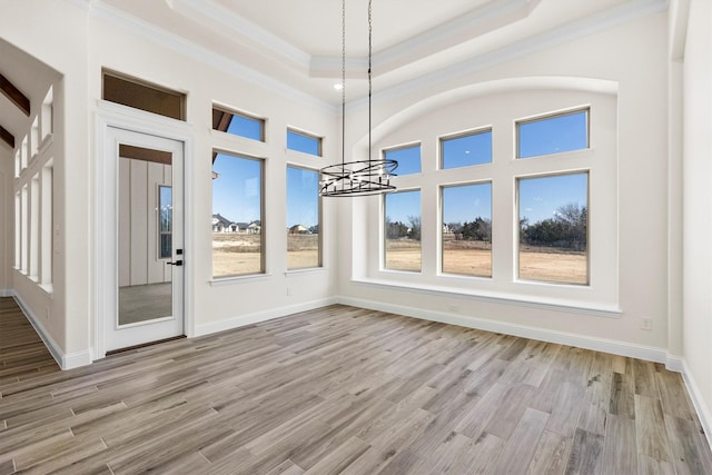 unfurnished dining area featuring ornamental molding, a raised ceiling, a chandelier, and light wood-type flooring