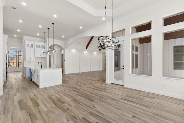 kitchen with decorative light fixtures, white cabinets, a center island with sink, and light hardwood / wood-style flooring