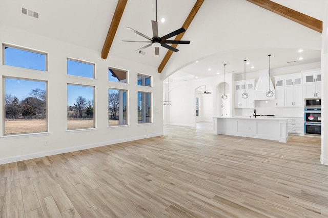 unfurnished living room featuring light hardwood / wood-style floors, sink, high vaulted ceiling, beam ceiling, and ceiling fan