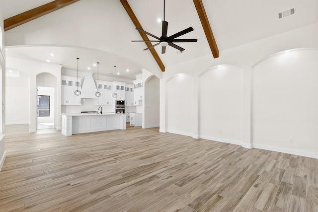 unfurnished living room with light wood-type flooring, ceiling fan, beamed ceiling, and high vaulted ceiling