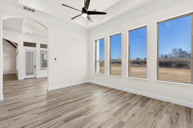 empty room featuring ceiling fan, light wood-type flooring, a tray ceiling, and ornamental molding