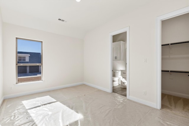 unfurnished bedroom featuring a walk in closet, lofted ceiling, a closet, light colored carpet, and ensuite bathroom