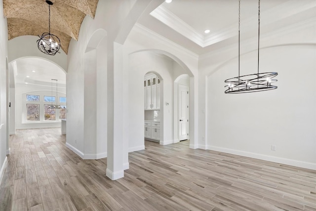 unfurnished dining area featuring crown molding, light wood-type flooring, lofted ceiling, and a notable chandelier