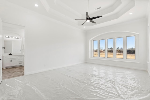 unfurnished bedroom featuring ceiling fan, connected bathroom, ornamental molding, and a tray ceiling