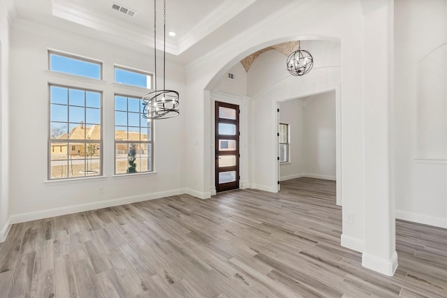 entryway with crown molding, a raised ceiling, a notable chandelier, and light wood-type flooring