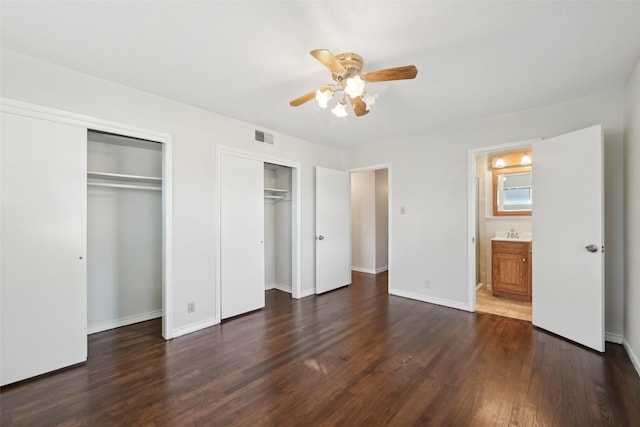 unfurnished bedroom featuring two closets, connected bathroom, sink, dark hardwood / wood-style floors, and ceiling fan