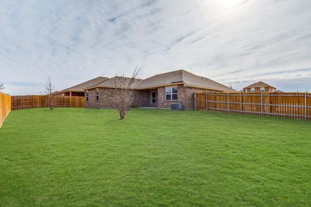 rear view of property with central AC, brick siding, a fenced backyard, and a lawn