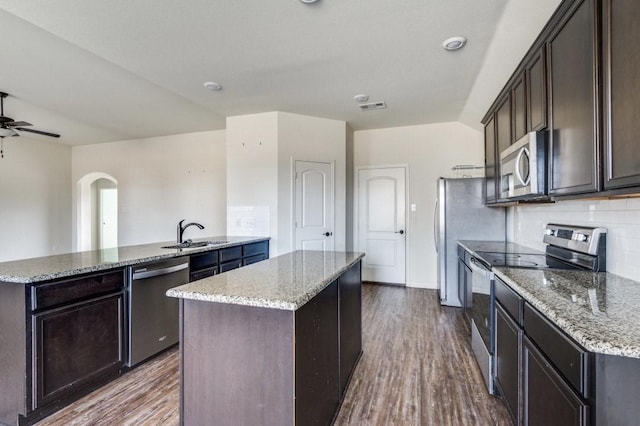 kitchen with appliances with stainless steel finishes, light stone counters, wood finished floors, a center island, and a sink