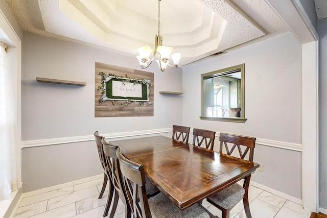 dining space featuring a chandelier, a textured ceiling, and a tray ceiling