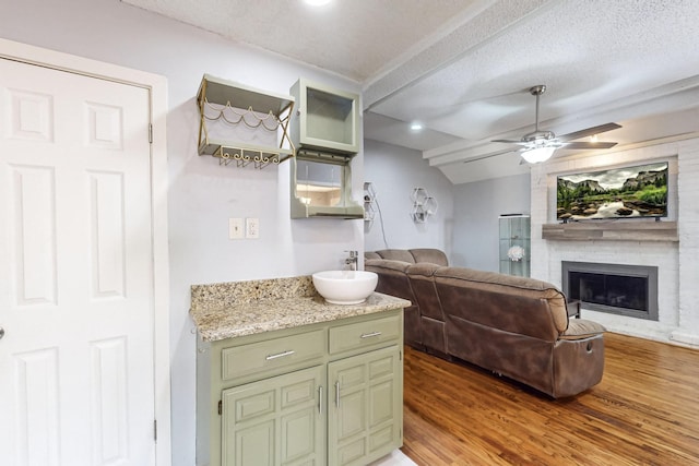 interior space with ceiling fan, hardwood / wood-style flooring, a brick fireplace, a textured ceiling, and green cabinetry